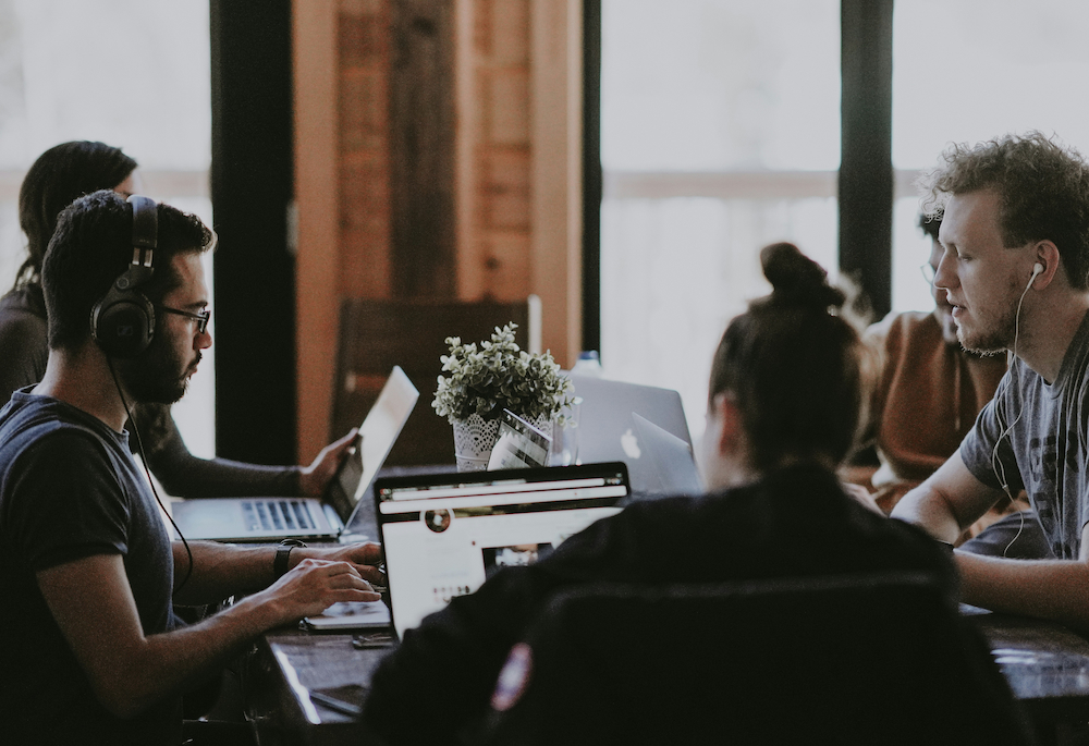 A group of creative professionals working on laptops in a collaborative studio setting, engaged in focused work and conversation