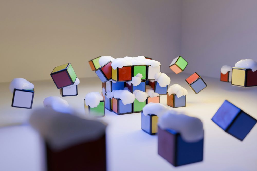 Colourful Rubik's cube pieces scattered and floating in mid-air with small white cloud puffs against a neutral background