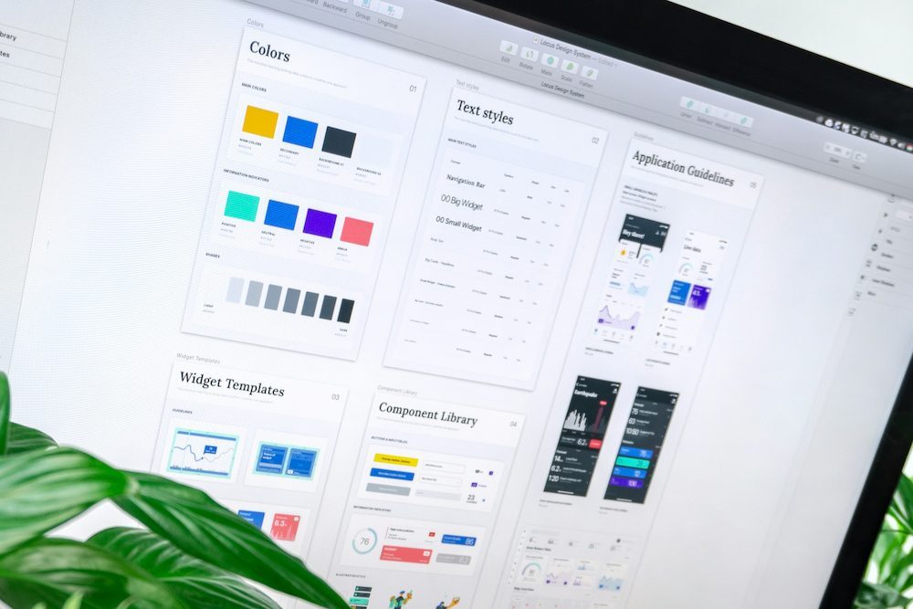 A monitor displaying a digital brand design system with colour swatches, text styles, widget templates, and component library panels