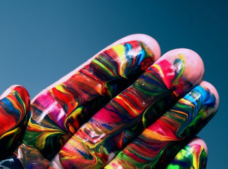 A hand covered in swirls of vibrant multicoloured paint against a teal background